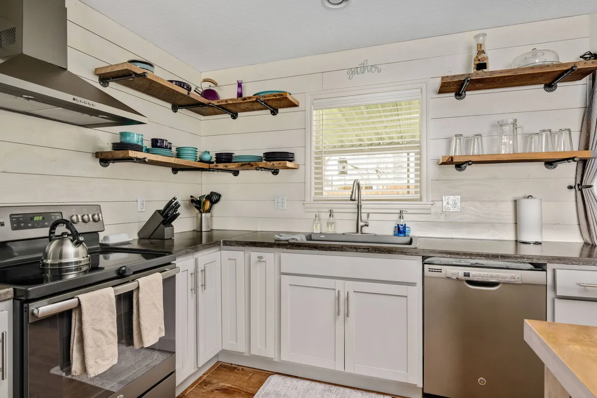 A modern kitchen with stainless steel appliances, open wooden shelving, and a large sink, designed for cooking and entertaining larger groups.