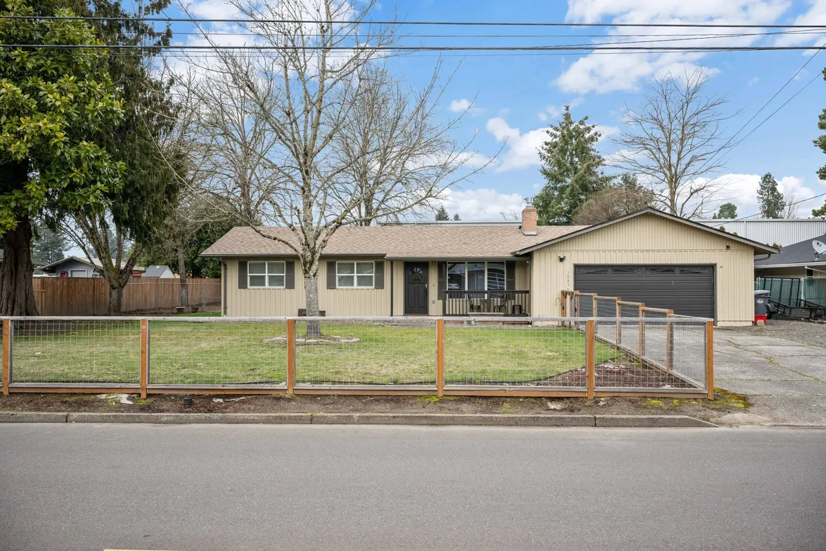 A friendly exterior view of the home featuring a spacious front porch, fenced yard, and garage. The setting suggests plenty of space for outdoor gatherings, kid play, and neighborhood connection.