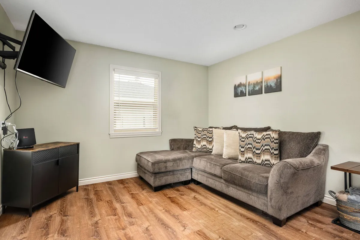 A cozy living room with a large sectional sofa, TV, and wall art—creating the ultimate spot for relaxing, watching movies, or catching up with friends and family. The layout encourages conversation and comfort, fitting for both downtime and engaging group activities.