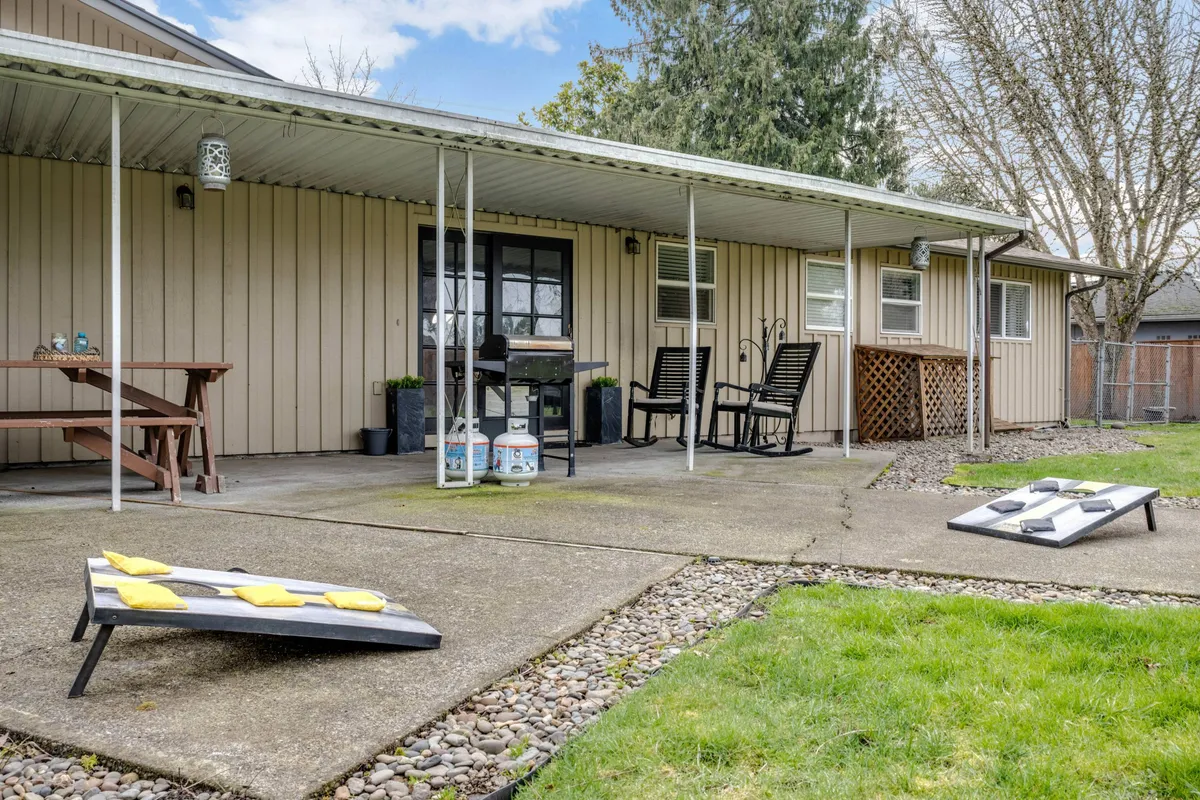 This image shows a well-appointed patio with seating, an outdoor table, and a cornhole game set up on the lawn. The setting is casual, ideal for sunset gatherings and friendly competitions, with plenty of room for relaxing or playing.