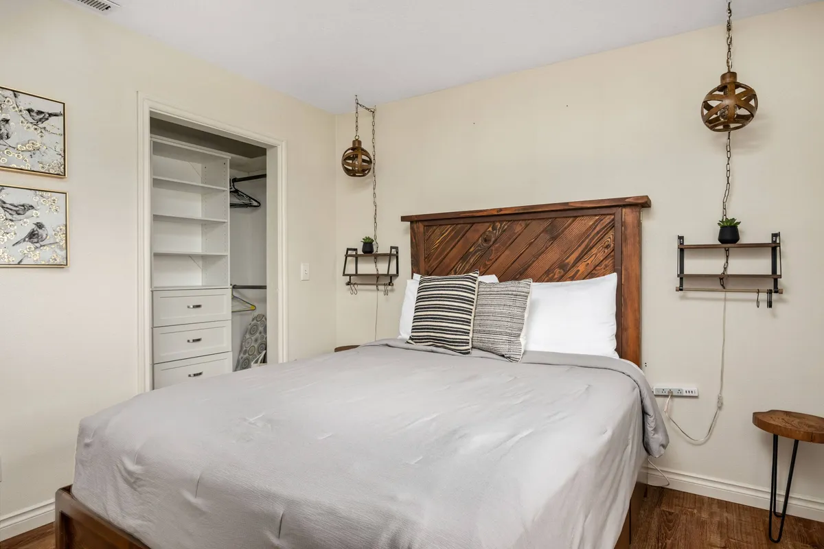 A peaceful bedroom scene with a wooden headboard, decorative pillows, and modern hanging light fixtures. The space is bathed in natural light, emphasizing its tranquil and restful ambiance.