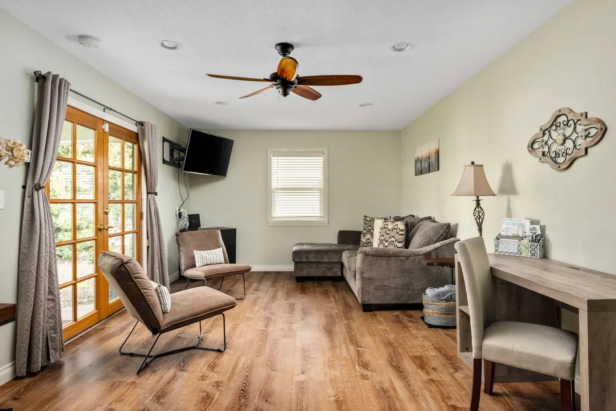 The image showcases a cozy, sunlit living area with a plush sofa, a welcoming dining table, elegant French doors letting in natural light, tasteful wall decor, and a comfortable chair. The space is perfectly set for relaxing, enjoying a morning coffee, working from home, or gathering with friends and family.