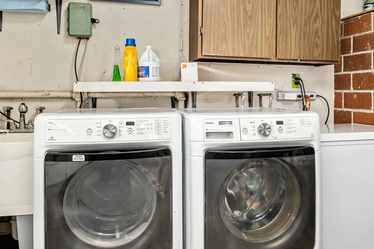 A practical laundry area with washing machines, wooden cabinets, and a shelf stocked with cleaning supplies. The scene is tidy and functional, emphasizing convenience for guests during extended stays.