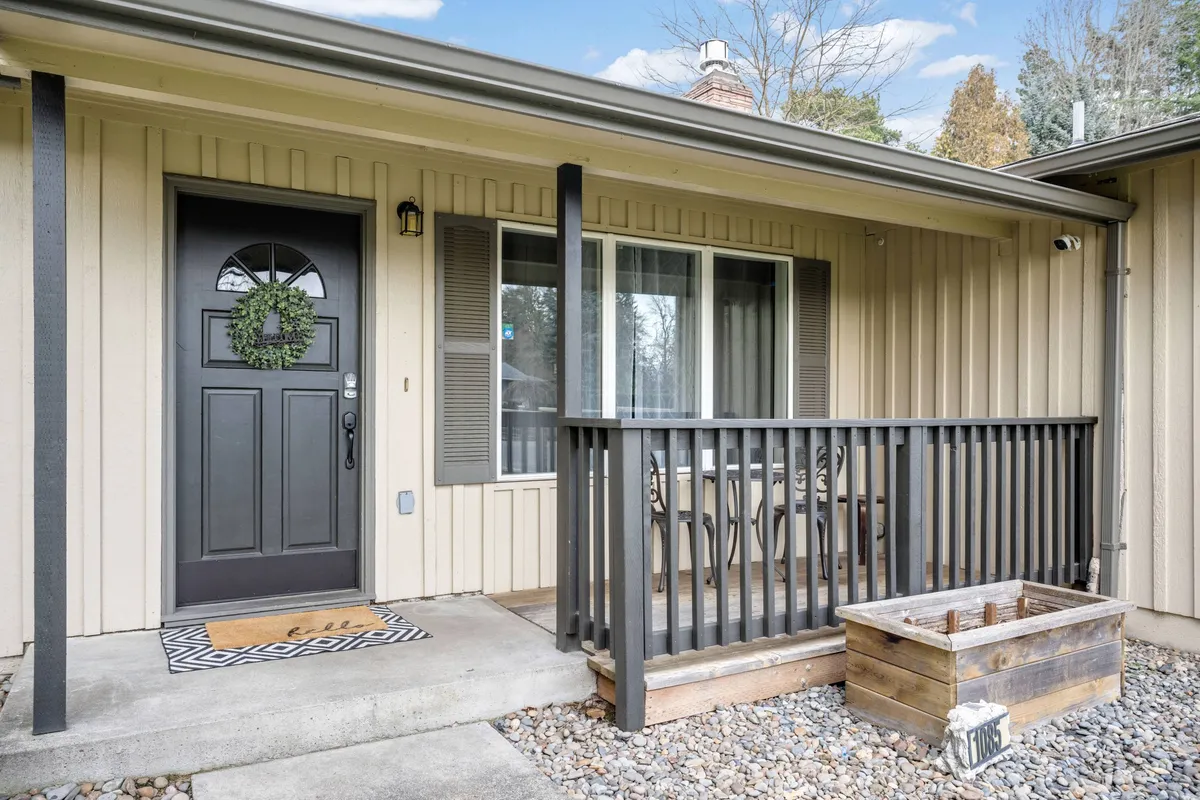 A close-up view of the home's inviting front porch, featuring a welcoming wreath on the door, a decorative mat, porch railing, and a planter box. The scene hints at a warm, approachable entry ideal for both arriving after a day's work and starting a morning commute.