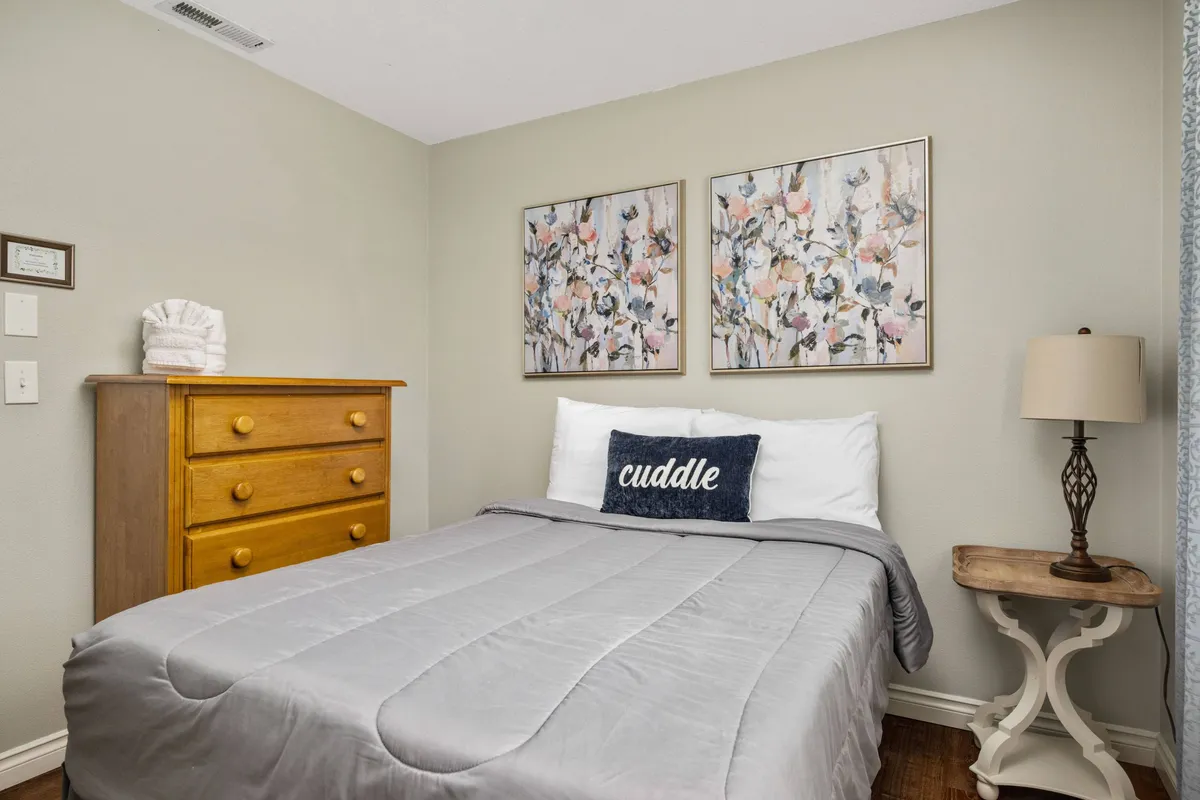 A welcoming bedroom with a cozy bed, wall art, nightstand, and dresser. The space feels private yet homey, with ample storage and warm accents that create an inviting atmosphere for relaxation.