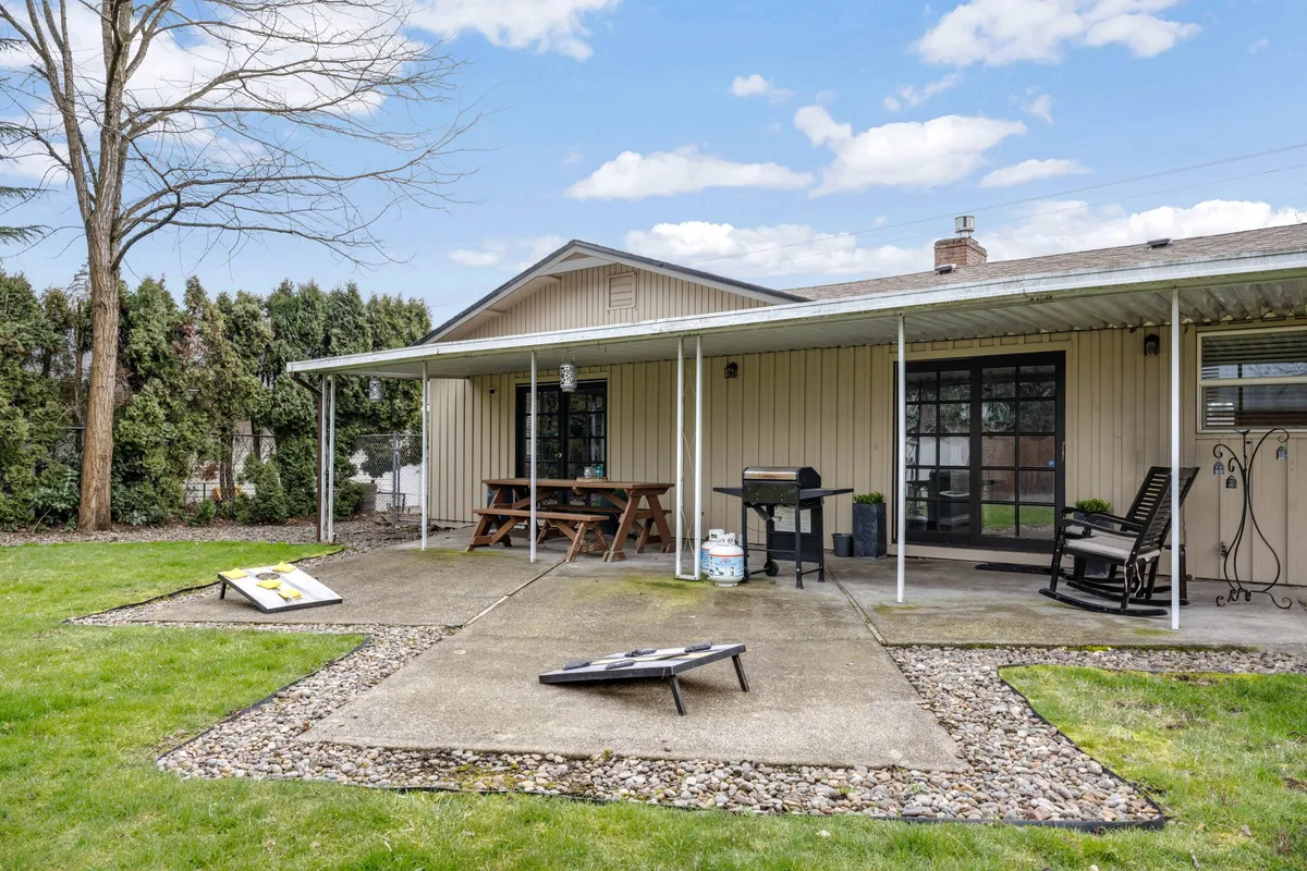This photo highlights a backyard patio equipped with comfortable furniture, a BBQ grill, a rocking chair, and a cornhole game board—inviting spaces for barbecuing, dining outdoors, and socializing. The area is casual and welcoming, ideal for family gatherings and celebrations.